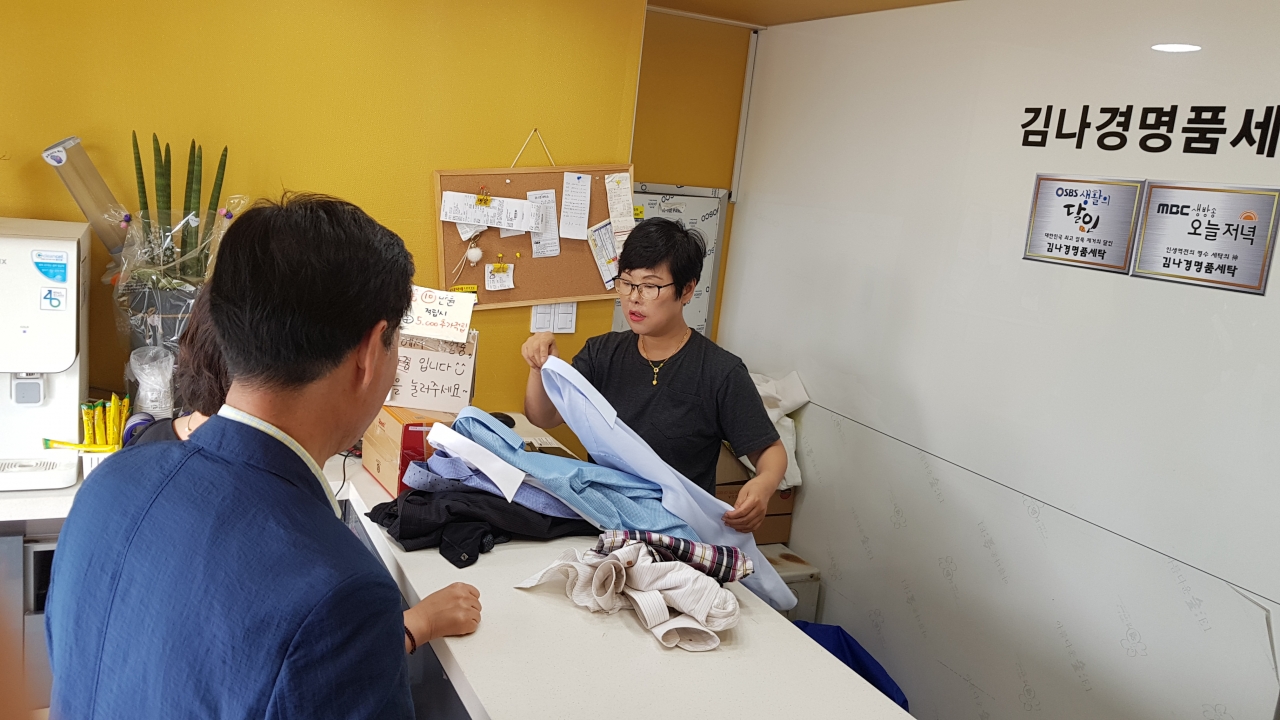 김나경 대표가 셔츠세탁을 맡기러 온 방문객에게 세탁이 진행되는 과정에 대해 설명하고 있다. / 안성수