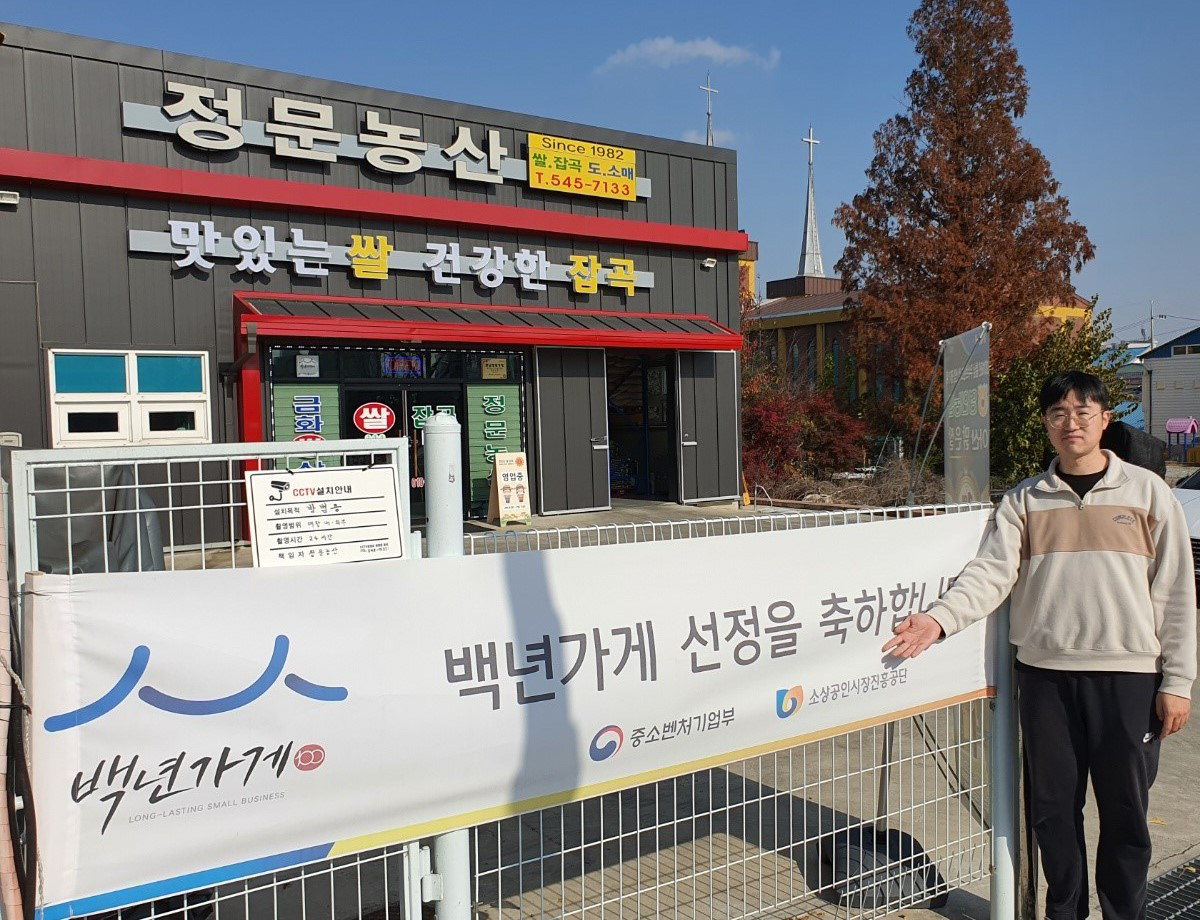 정문농산 가게를 이끌고 있는 김정문 씨가 가게앞에서 백년가게 선정을 기념하고 있다.